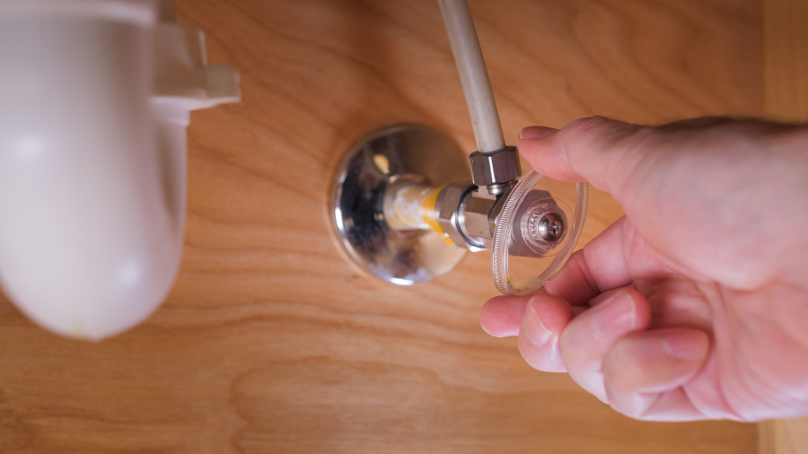 A bathroom water shut-off valve under a bathroom sink. A hand is turning off the shut-off valve. Son-Rise plumbing can replace valves like this that wear out and leak over time.